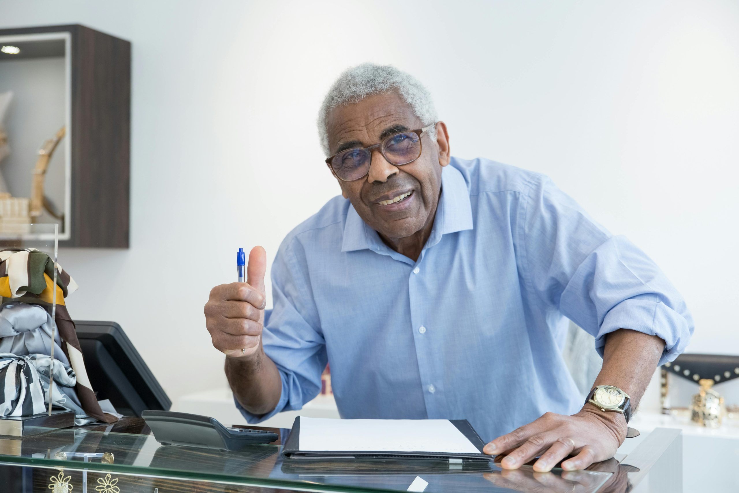 Cheerful elderly man giving a thumbs up at a desk, emphasizing positivity and confidence.